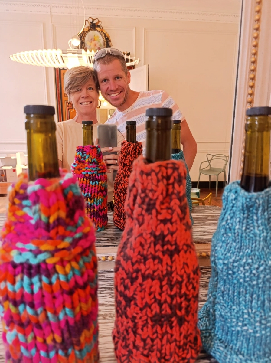 Véro et Cédric, souriants, derrière des bouteilles habillées de chaussettes en laine