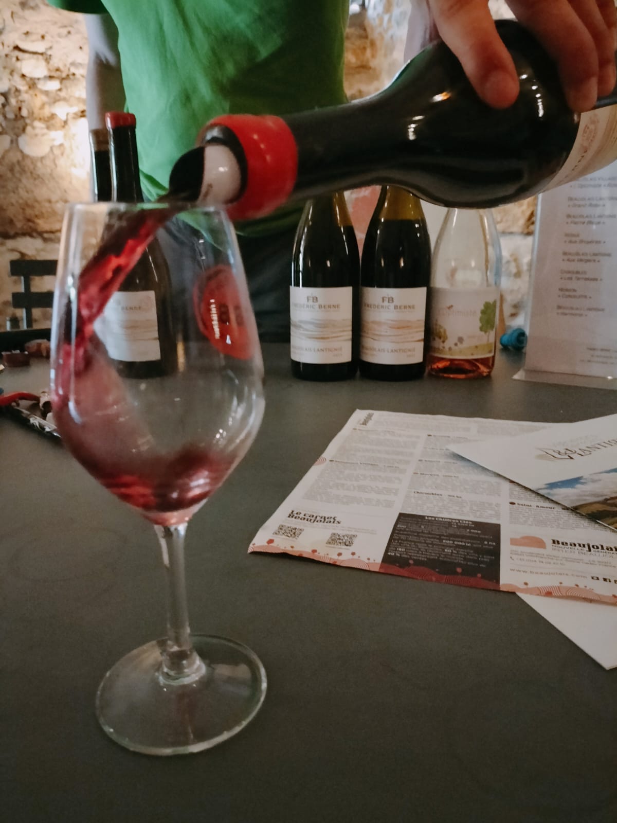 Un vigneron servant un vin rouge dans le caveau, cartes de domaines posées à côté